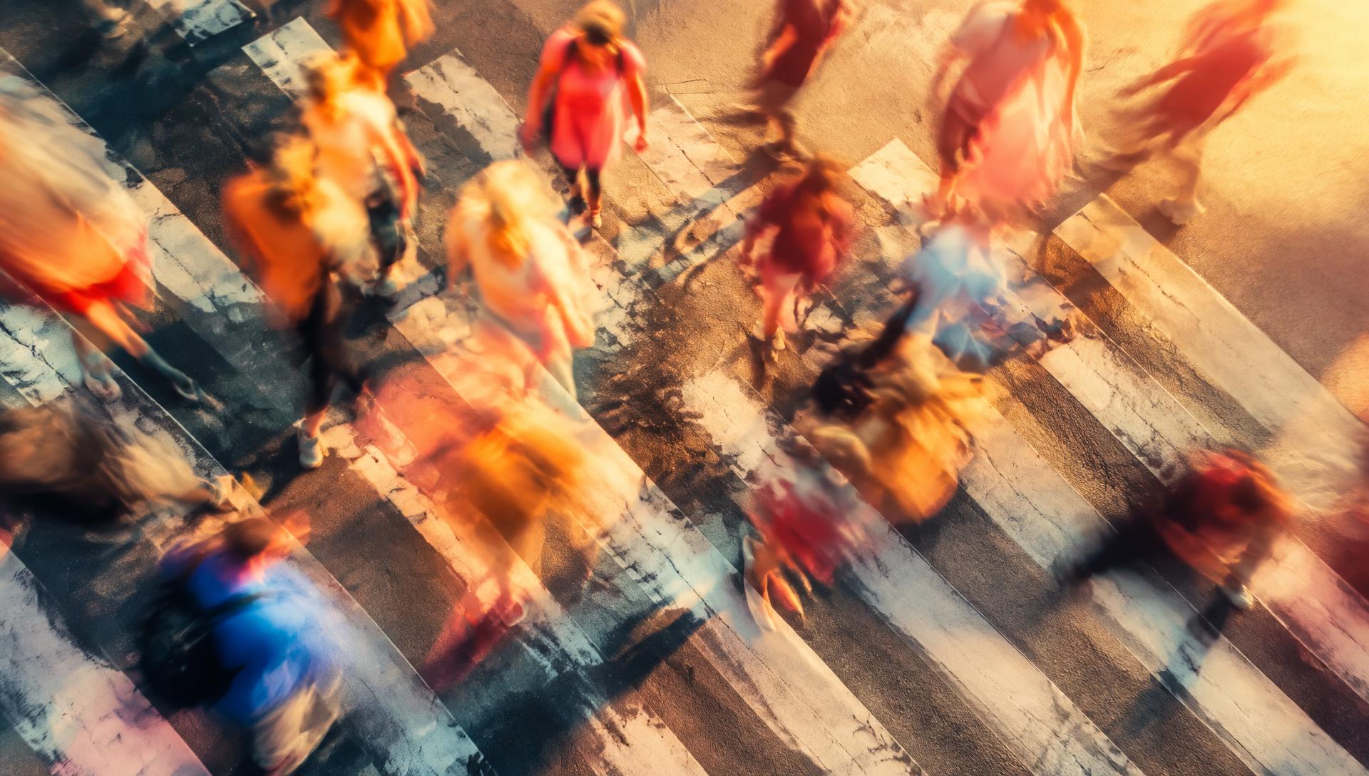 Long-exposure view of people in motion crossing a city street at sunset